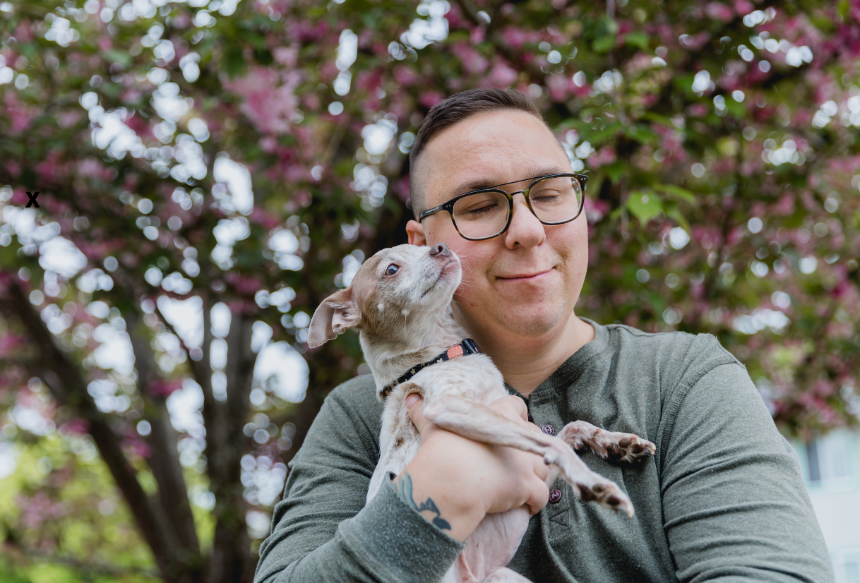 Adult smiling while holding a small dog outdoors under a blossoming tree